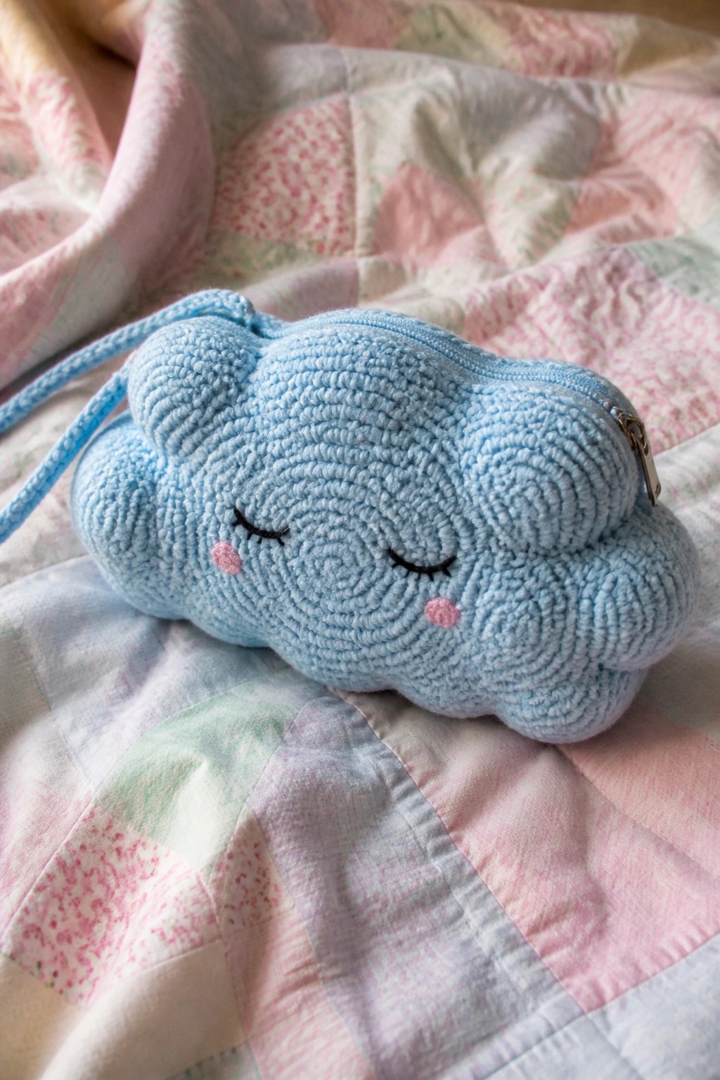 Blue cloud-shaped zippered pouch with sleepy face on pastel patchwork quilt.