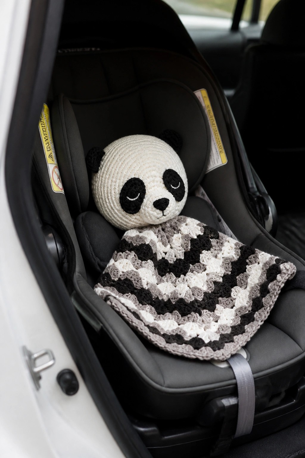 Crocheted panda toy with striped blanket in black infant car seat