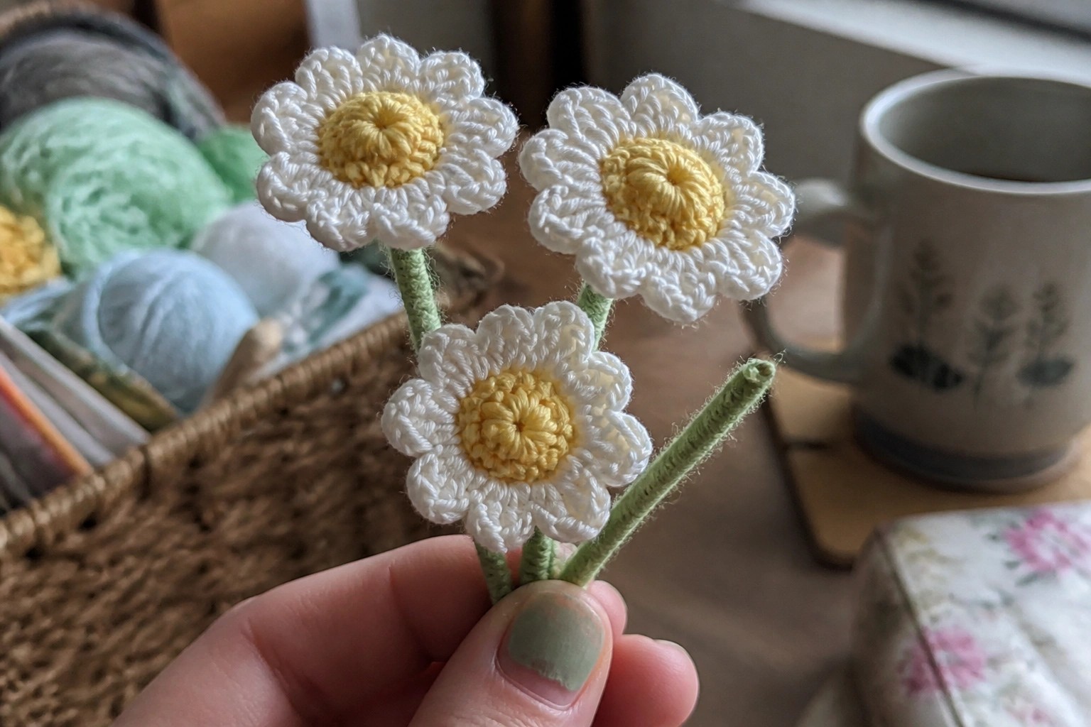 Hand holding three white crocheted flowers with yellow centers on green stems