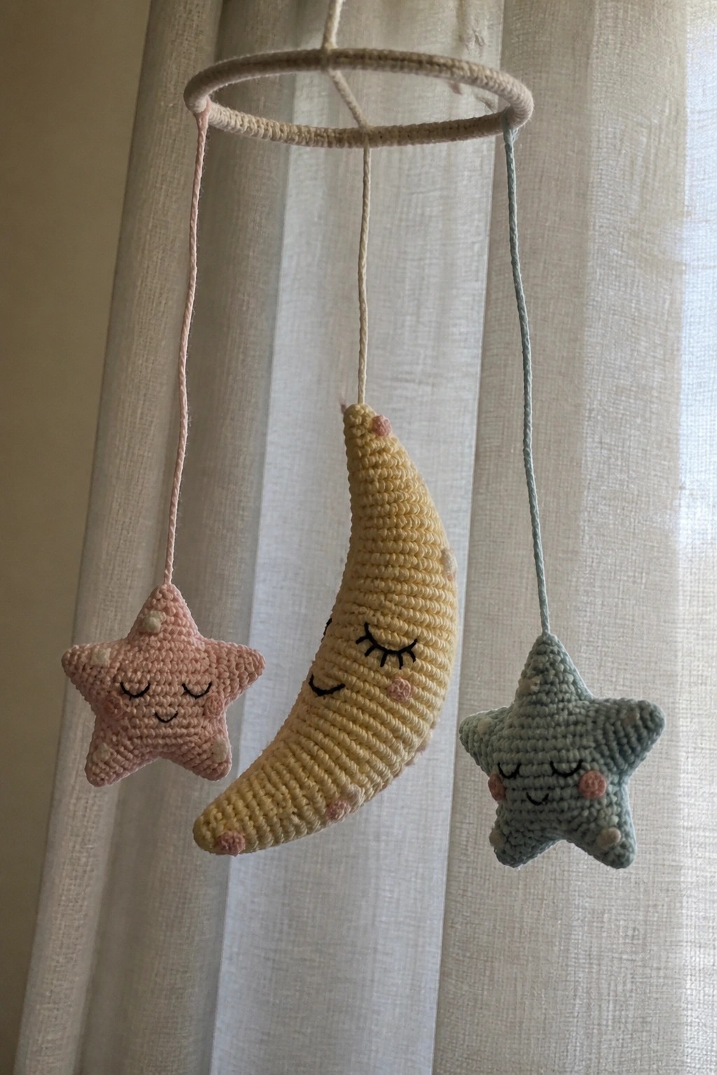 Crocheted pink star, yellow crescent moon, and teal star mobile on ring