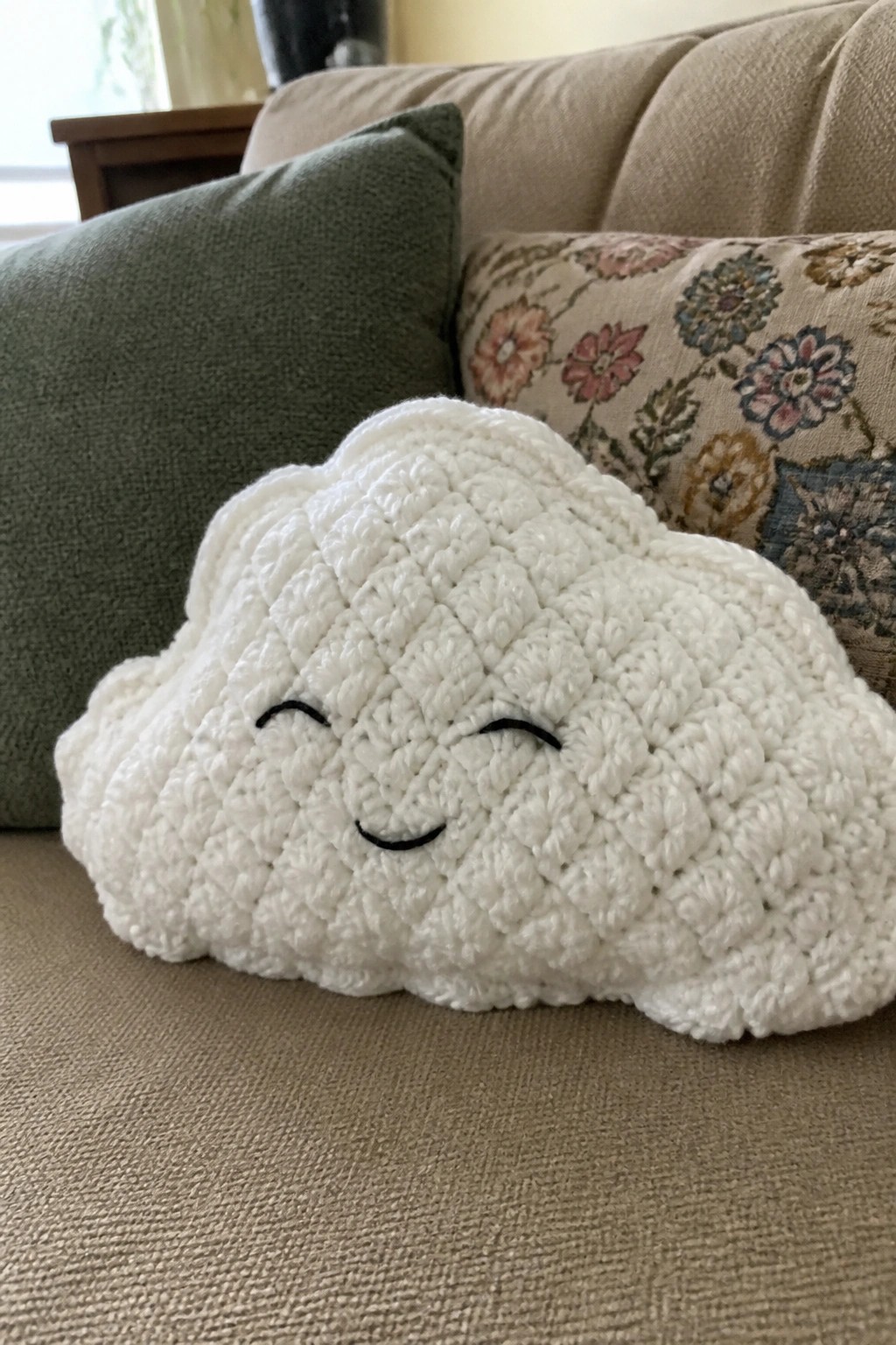 White crocheted cloud plush with smiling face on beige couch with pillows