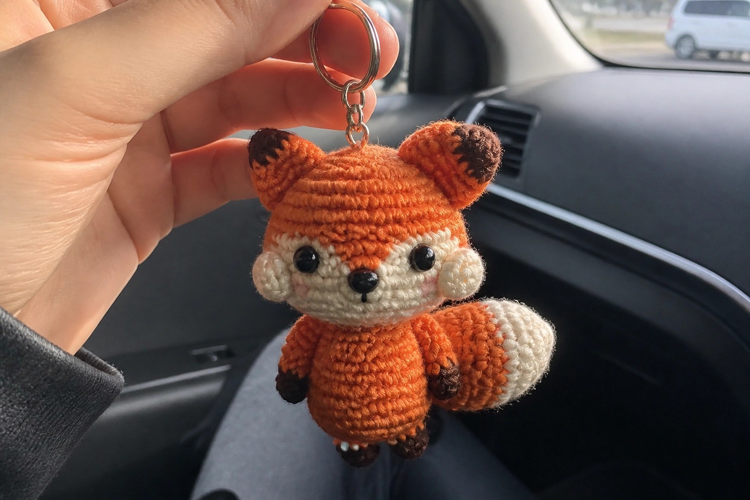 Hand holds orange crocheted fox keychain with white muzzle on metal chain.
