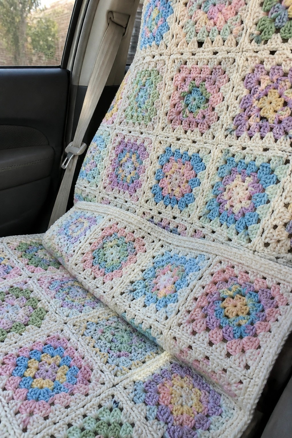 Pastel crocheted granny square blanket draped over a car seat