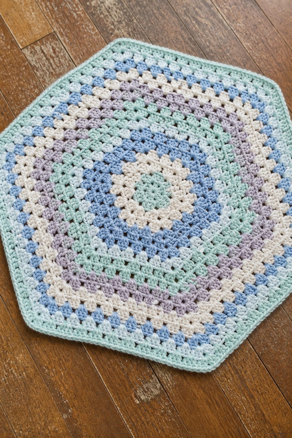 Pastel crocheted hexagonal mat with blue, purple, and mint patterns on wood.