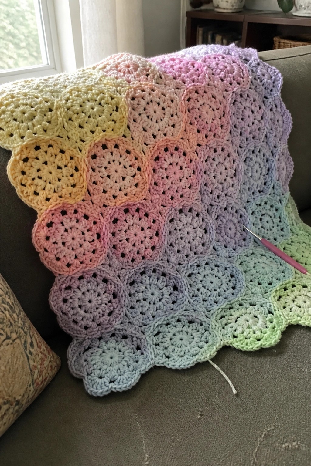 Rainbow crocheted blanket with circular motifs draped on gray couch beside hook