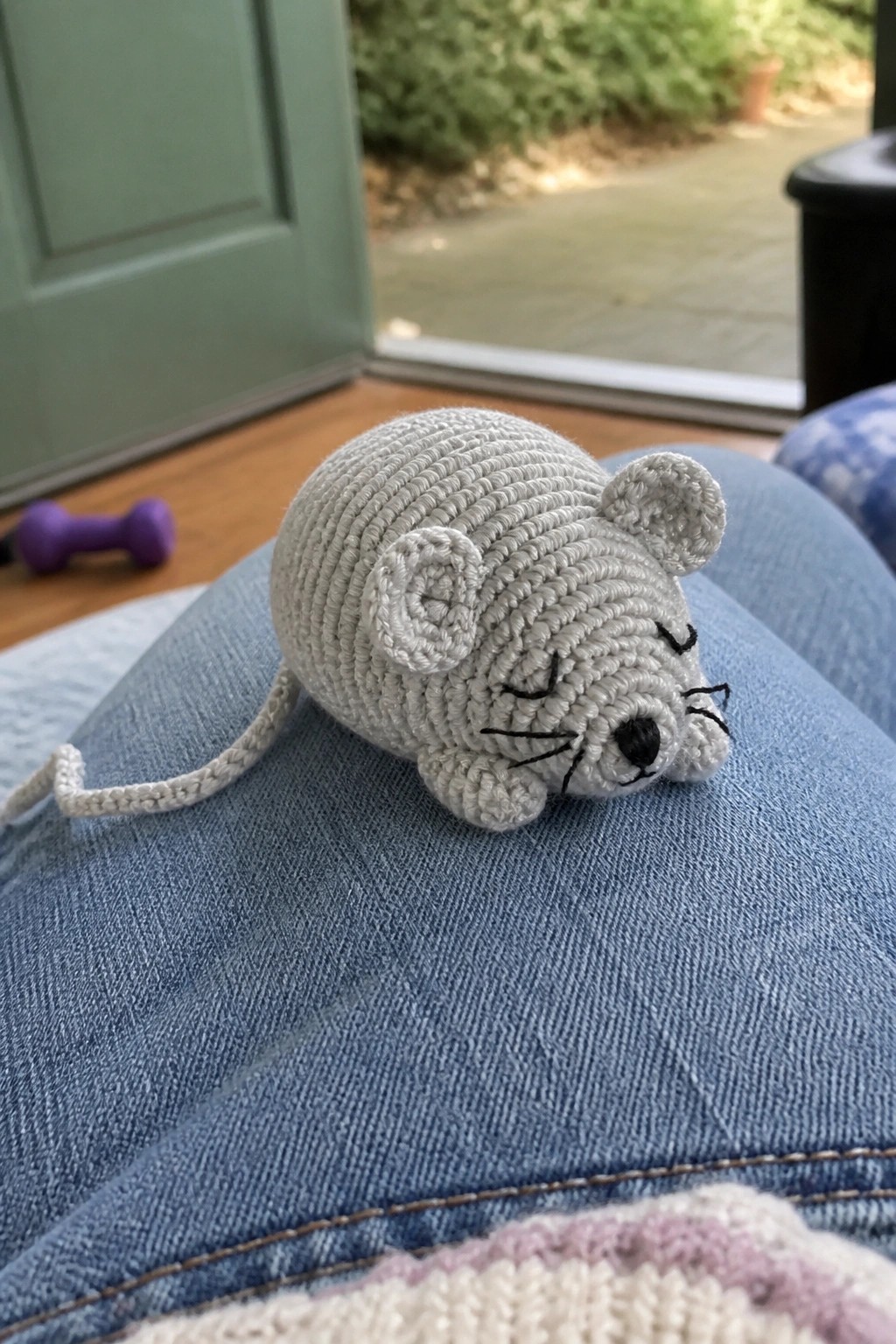 Gray crocheted mouse with closed eyes resting on blue denim jeans