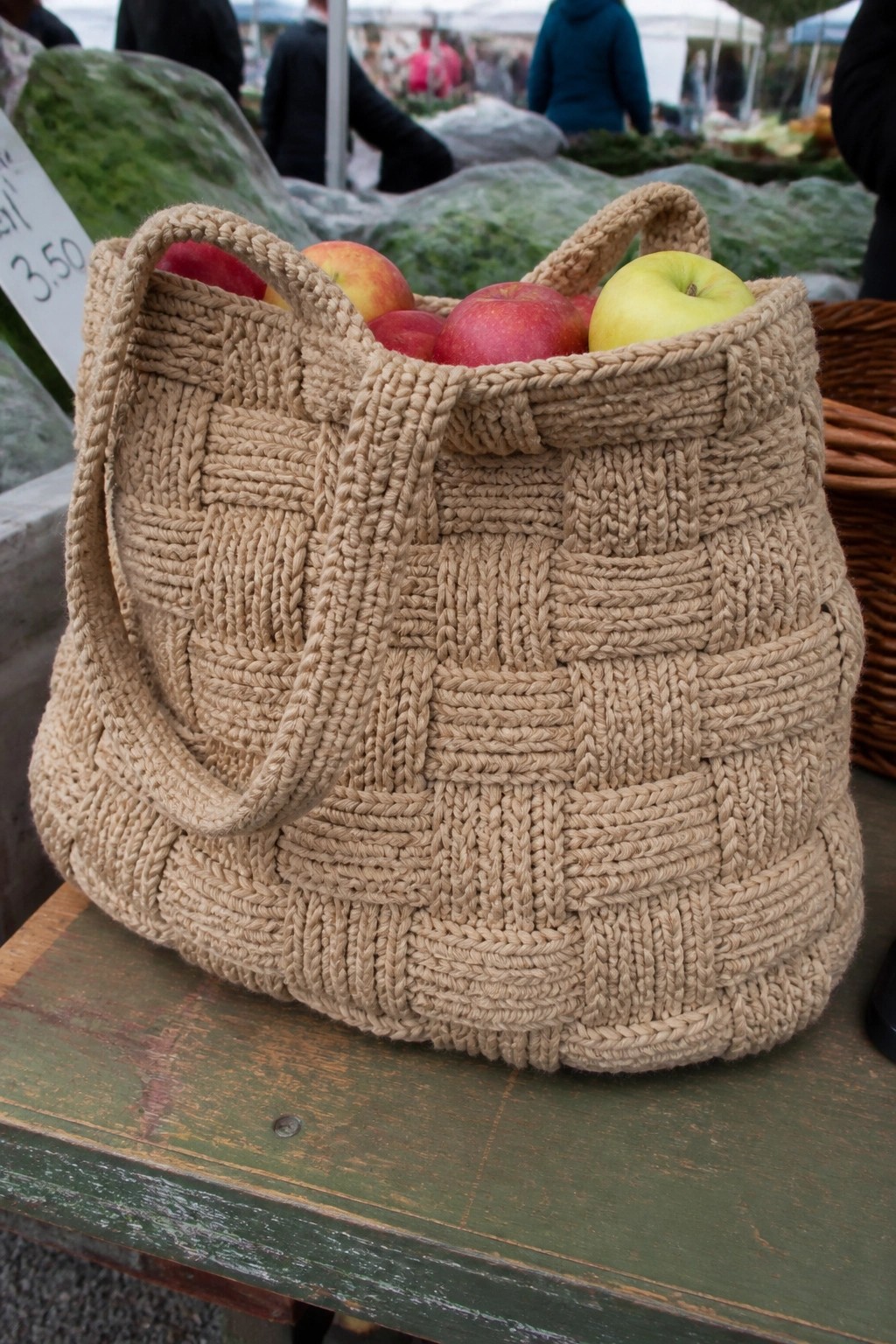 Woven beige tote bag holding red and green apples on weathered green wooden table