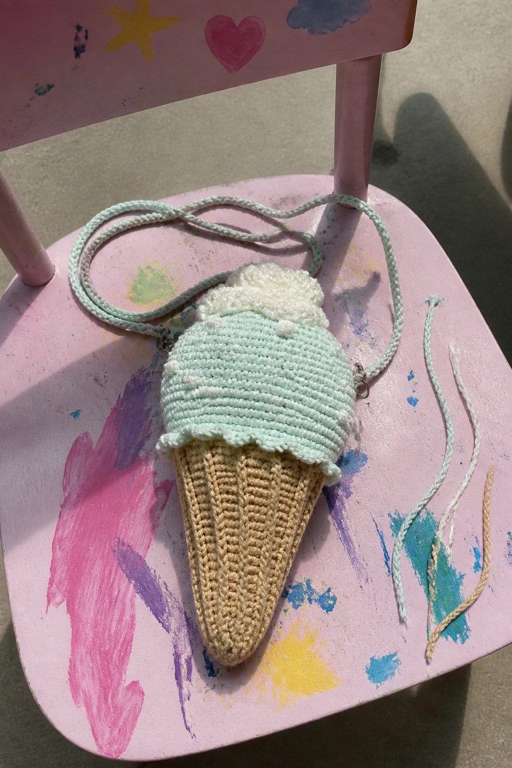 Crocheted mint green ice cream cone bag on paint-splattered pink chair