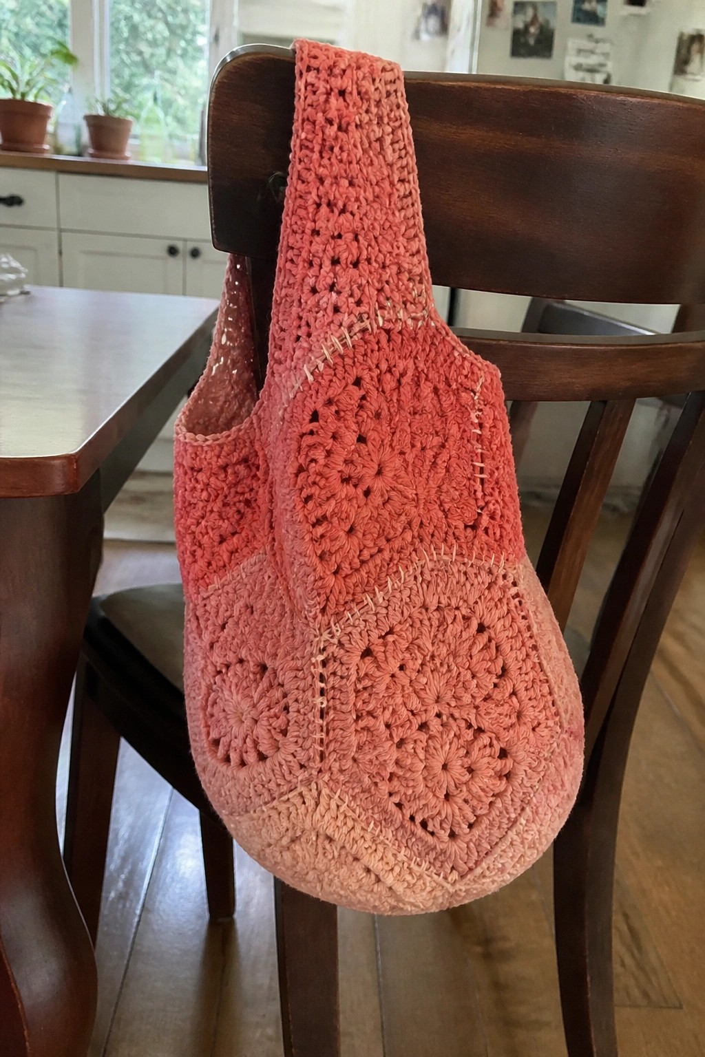 Pink ombre crocheted bag hanging on back of wooden dining chair.