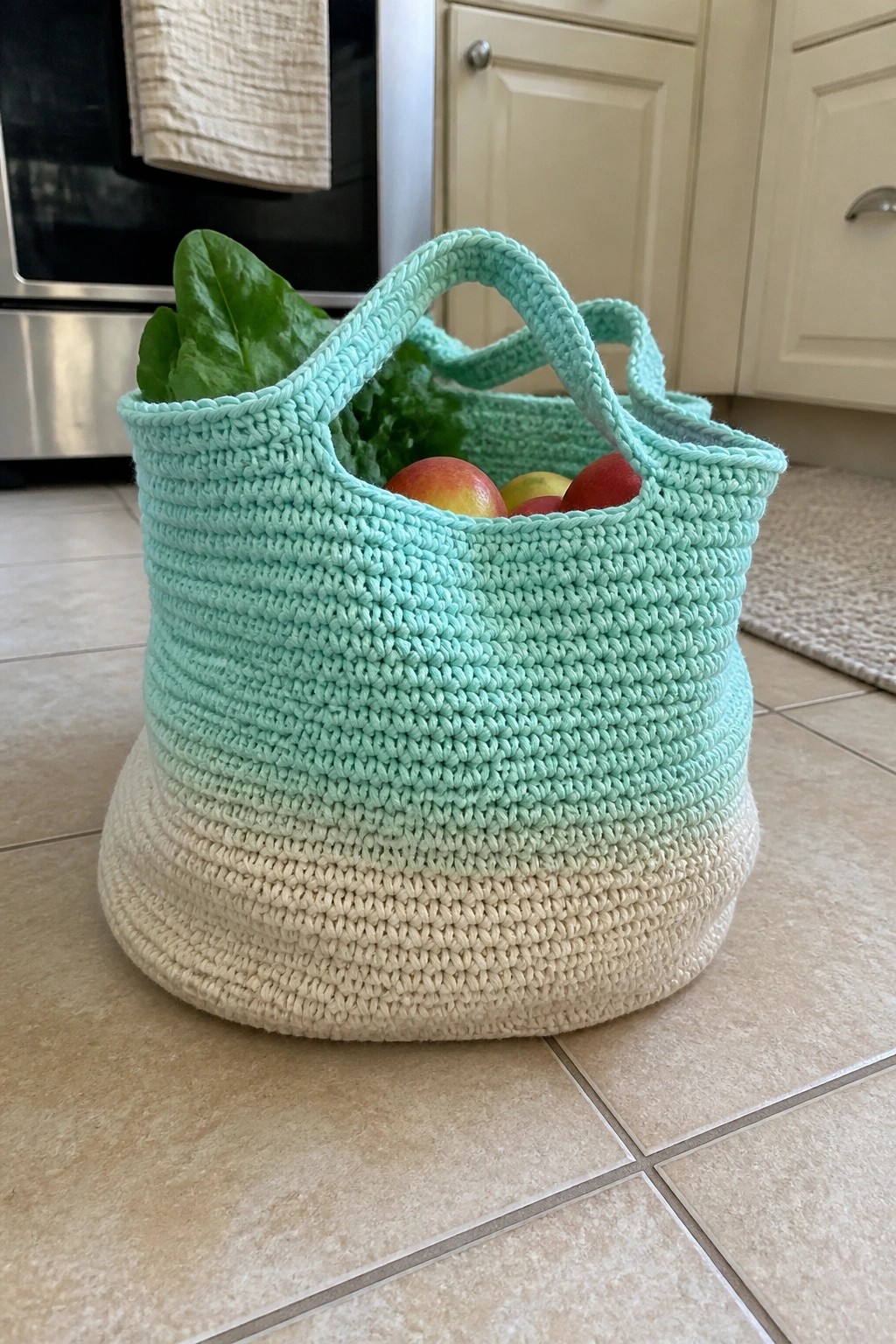 Mint green and cream crocheted basket holding apples and greens on kitchen floor