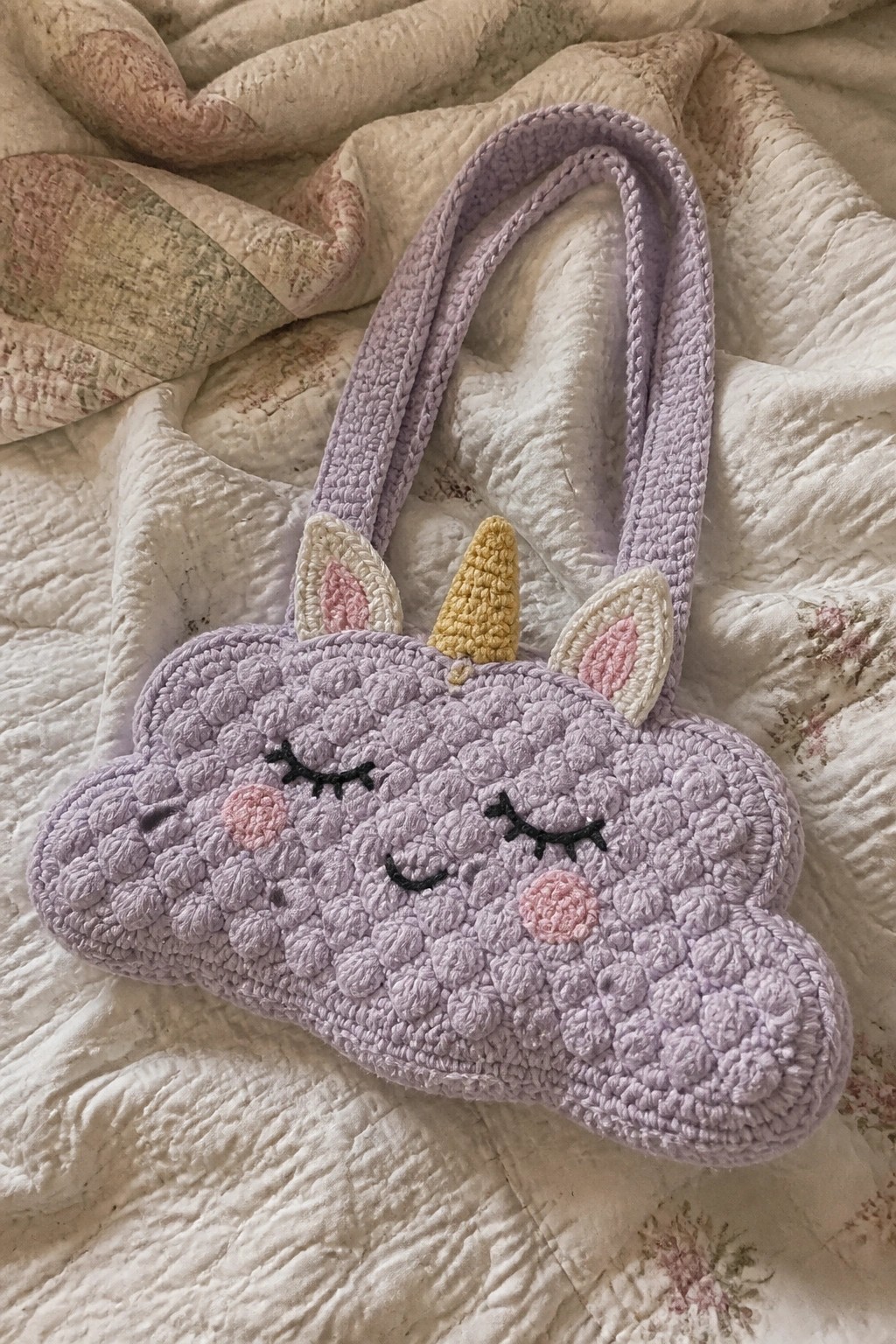 Crocheted lavender unicorn bag with yellow horn and embroidered face on quilt.