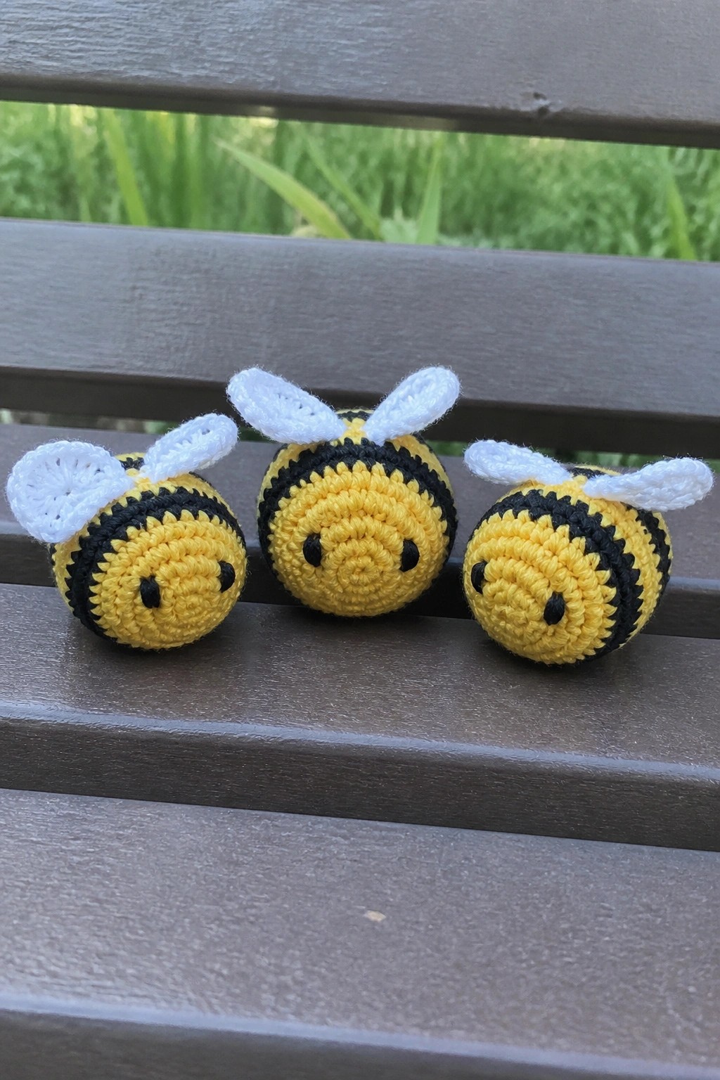 Three crocheted yellow bees with black stripes and white wings on a bench.