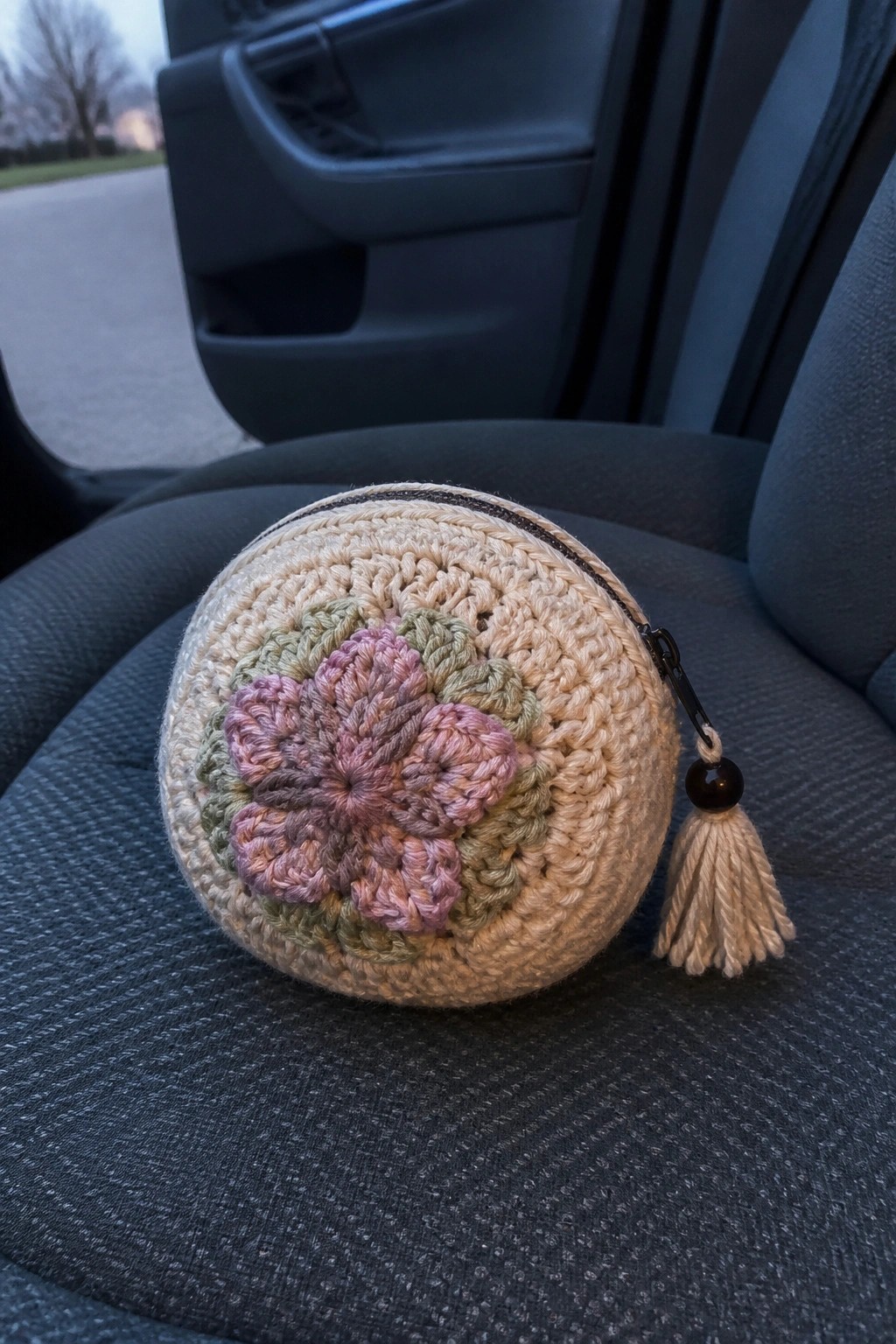 Crocheted beige pouch with pink flower and tassel on gray car seat