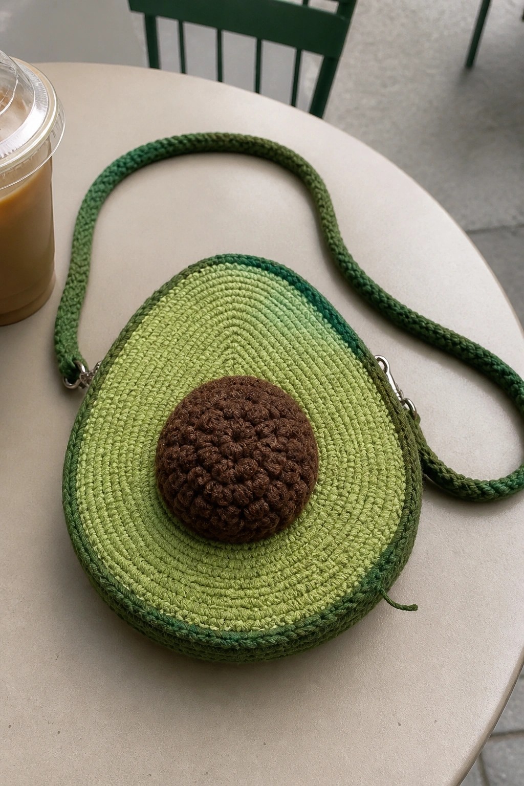 Crocheted avocado-shaped bag with brown pit and green strap on cafe table