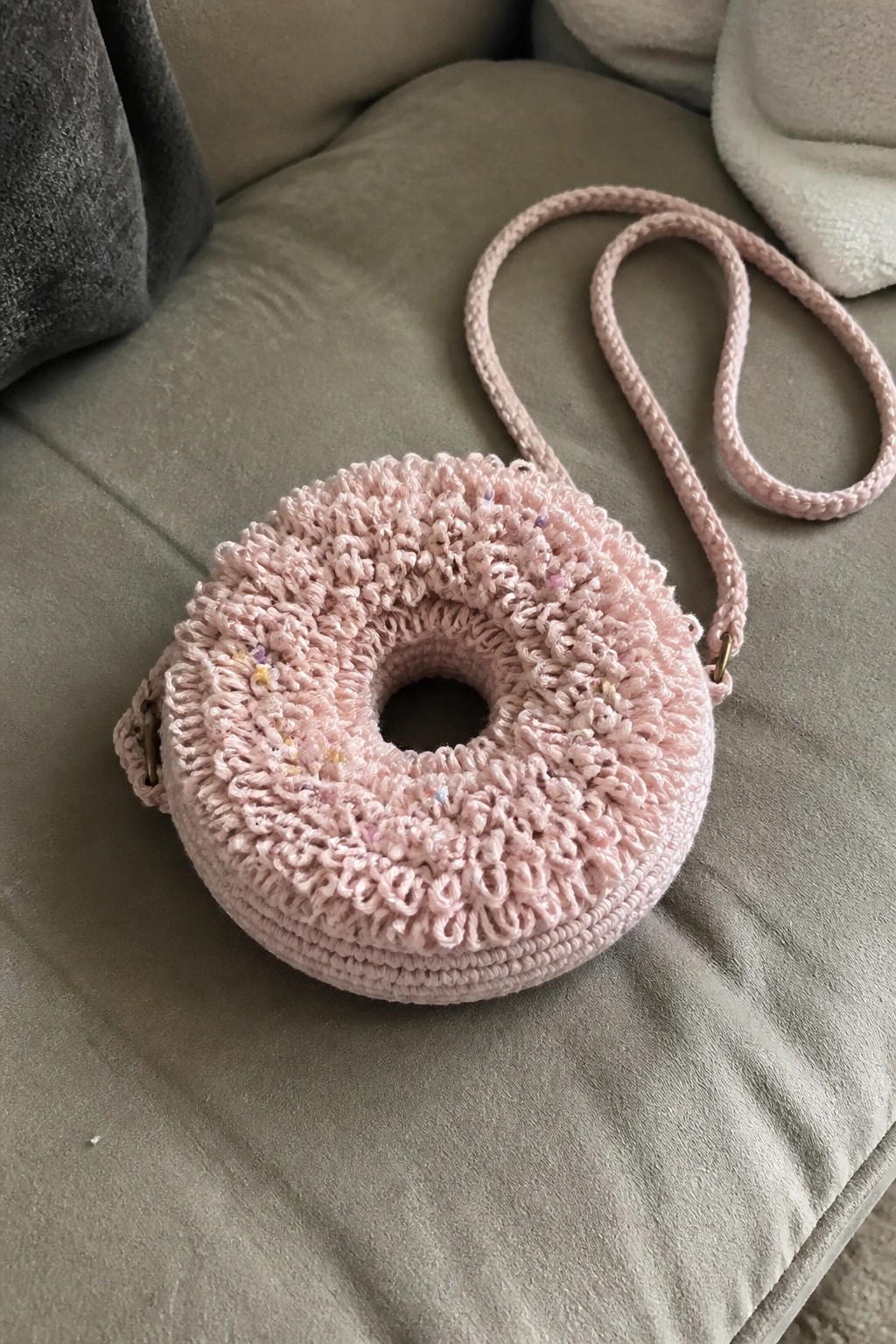 Pink crocheted donut-shaped bag with braided strap on gray couch