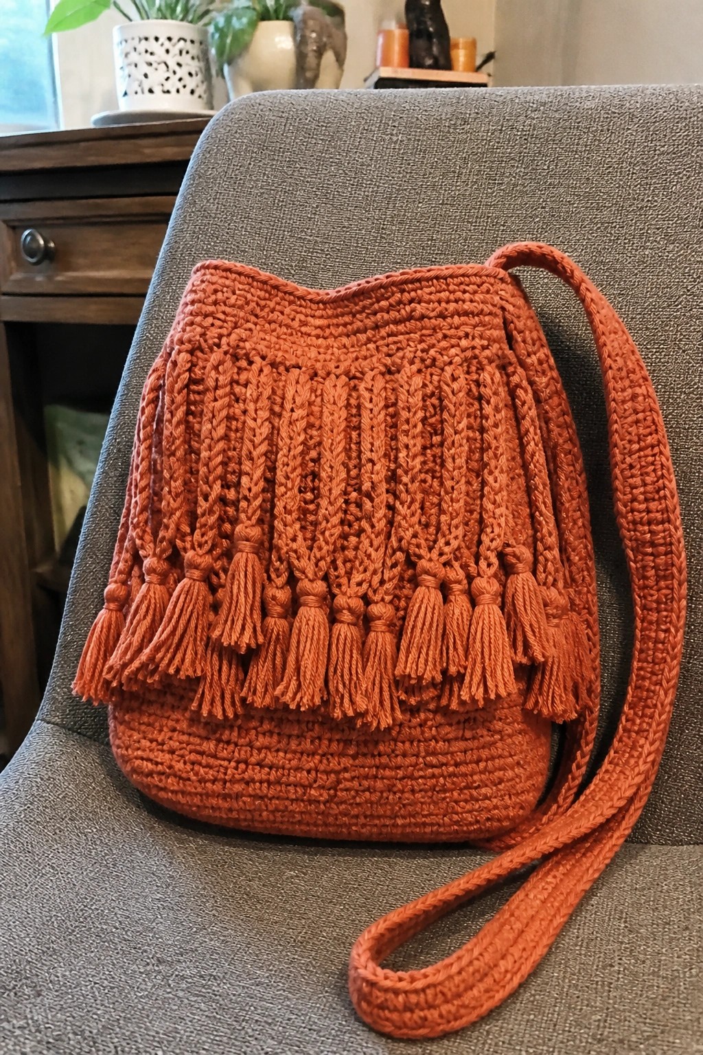 Orange crocheted bucket bag with tassels on gray upholstered chair