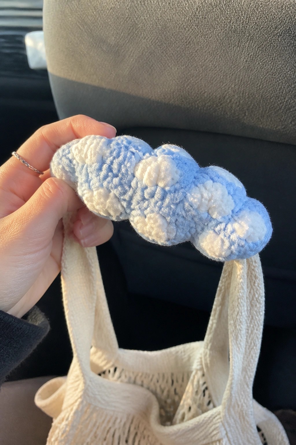 Hand holding blue and white plush crocheted chain over beige woven tote in car