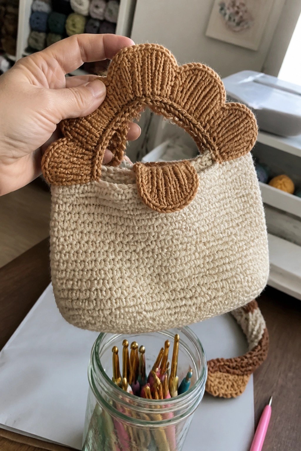 Hand holding beige crocheted bag with brown scalloped handles above hook jar
