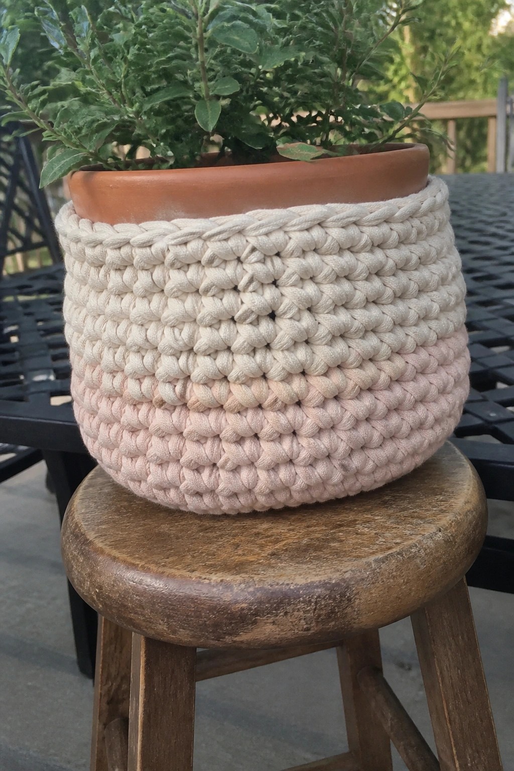 Cream and pink crocheted basket holding potted plant on wooden stool
