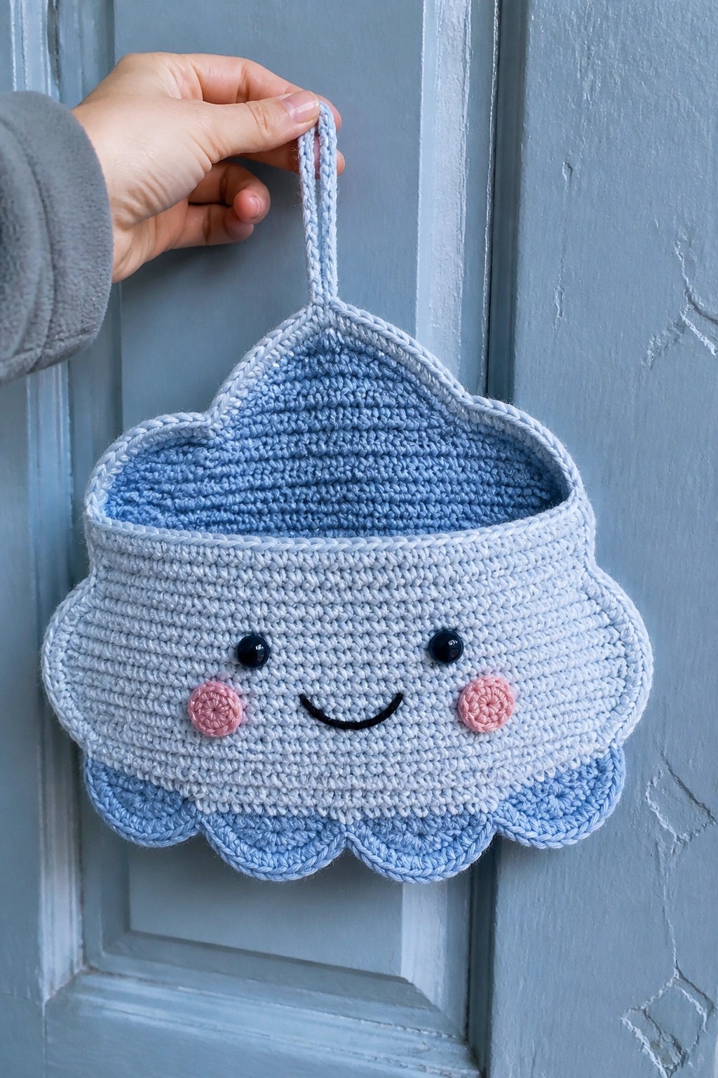 Hand holding light blue crocheted cloud basket with smiling face on door