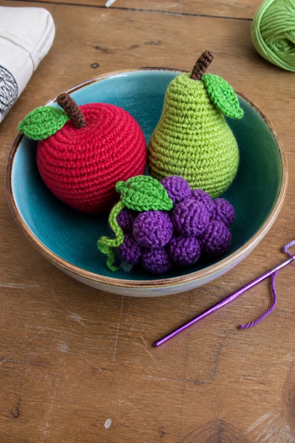 Crocheted red apple, green pear, and purple grapes in turquoise bowl with hook