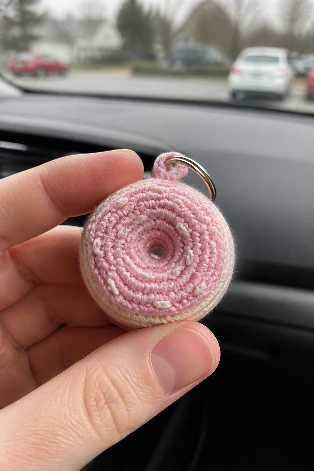Hand holding pink and white crocheted donut keychain with metal ring in car