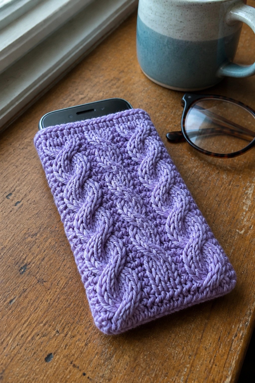 Purple cable-knit phone case on wooden table with mug and glasses