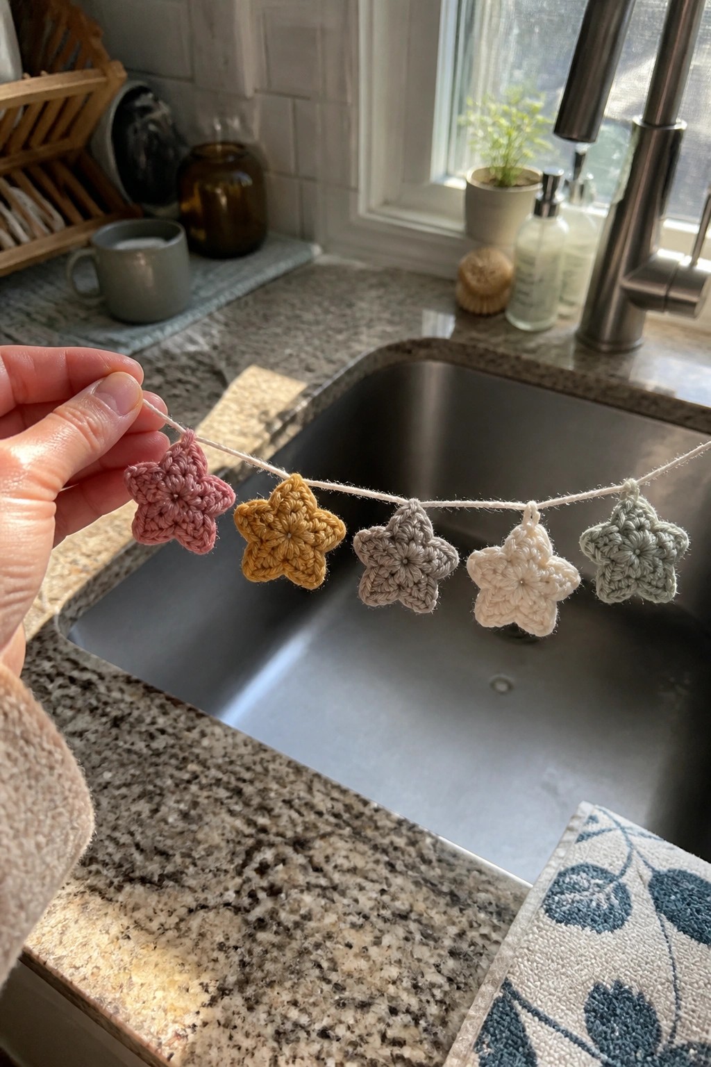 Hand holding colorful crocheted star garland over kitchen sink and granite counter.