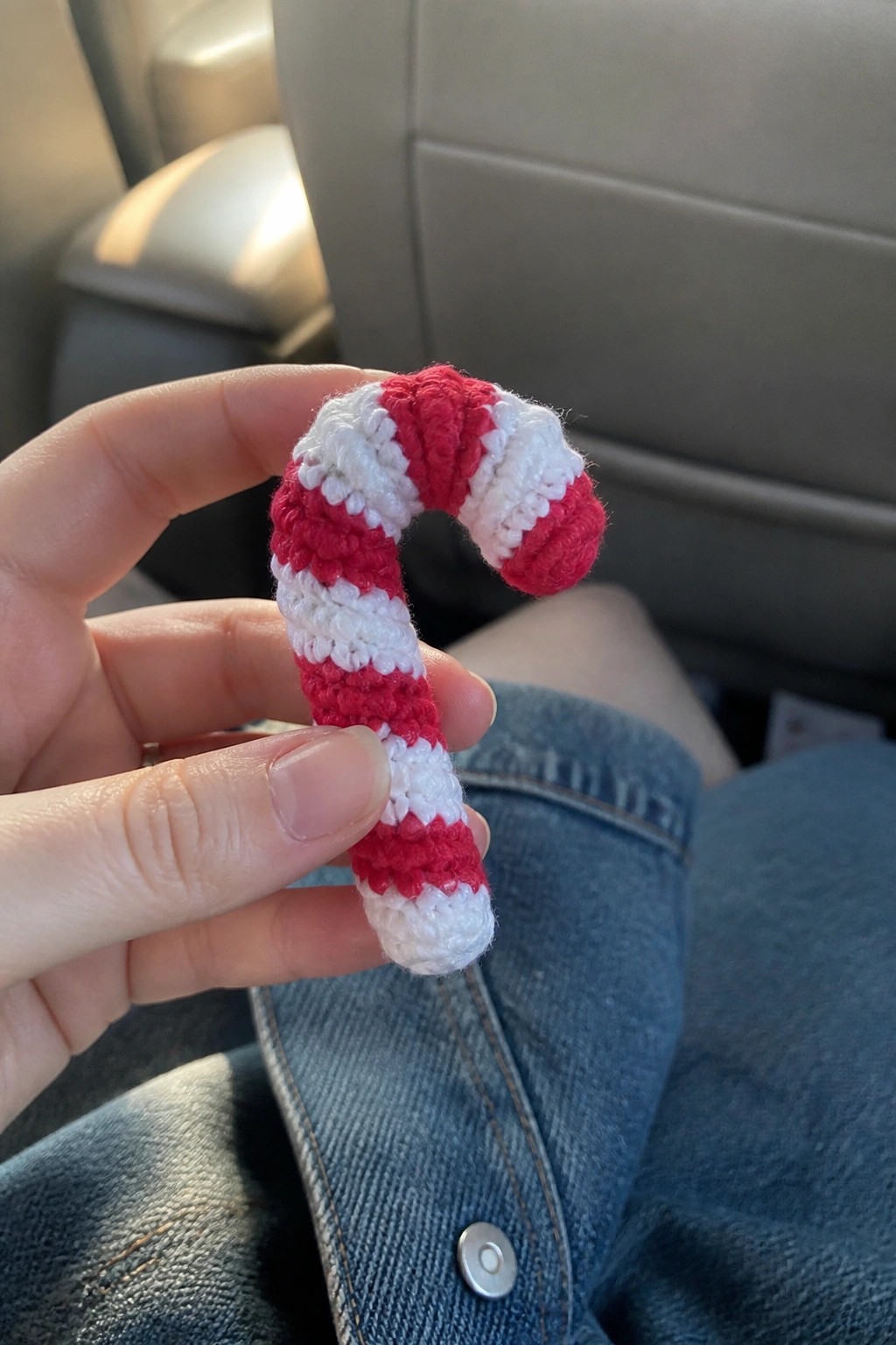 Hand holding red and white crocheted candy cane above blue denim jeans.