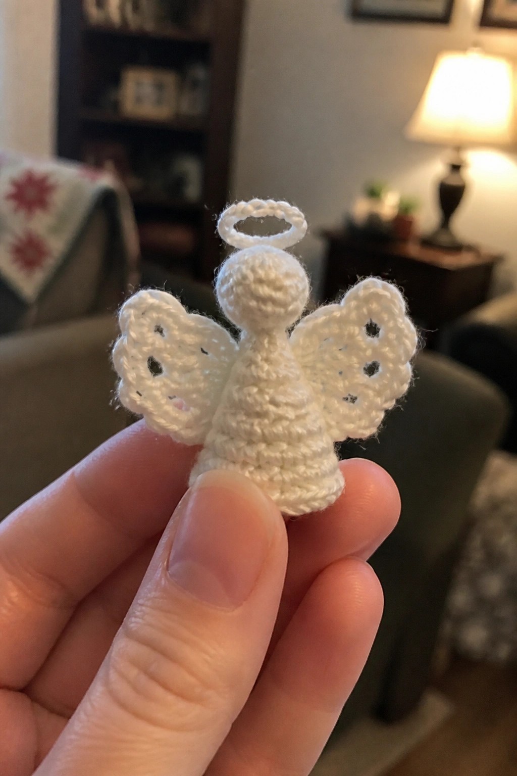 A hand holds a small white crocheted angel with wings and a halo.