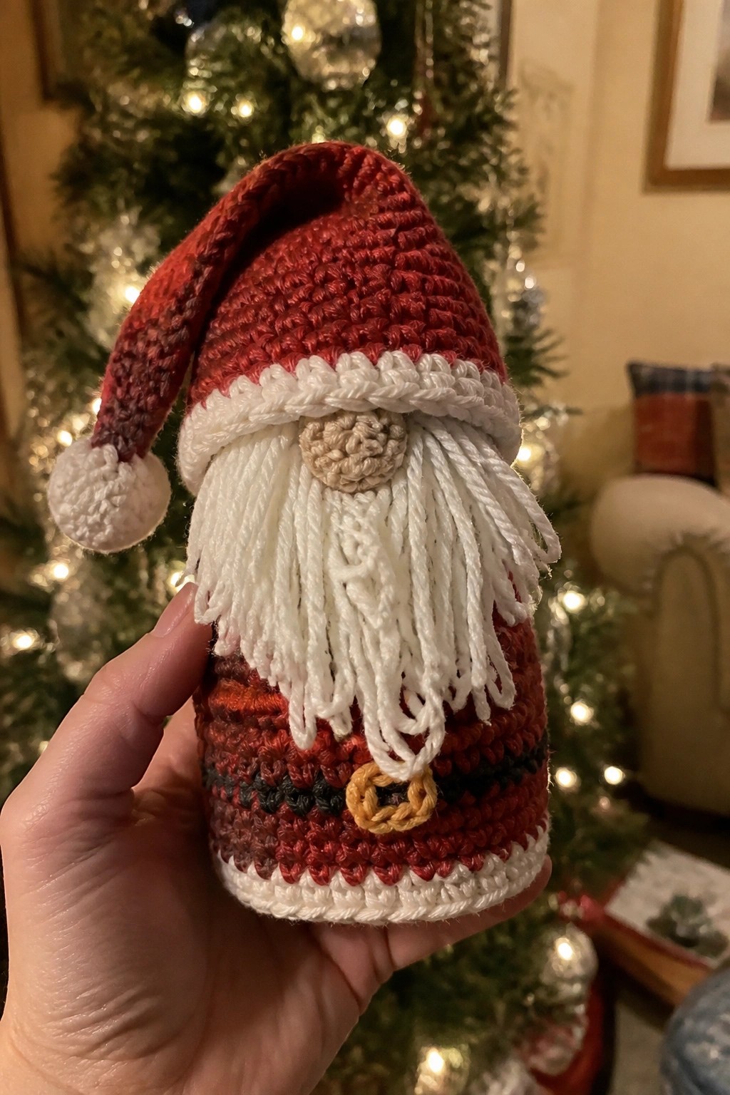 Hand holding crocheted Santa gnome with red hat, white beard, and striped body.