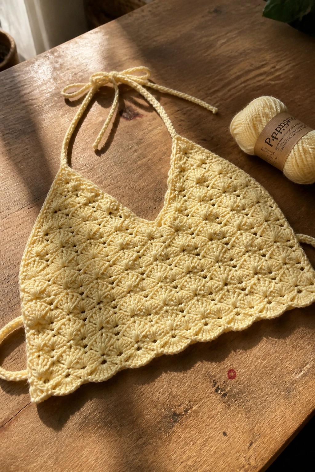 Yellow crocheted halter top with yarn on sunlit wooden table