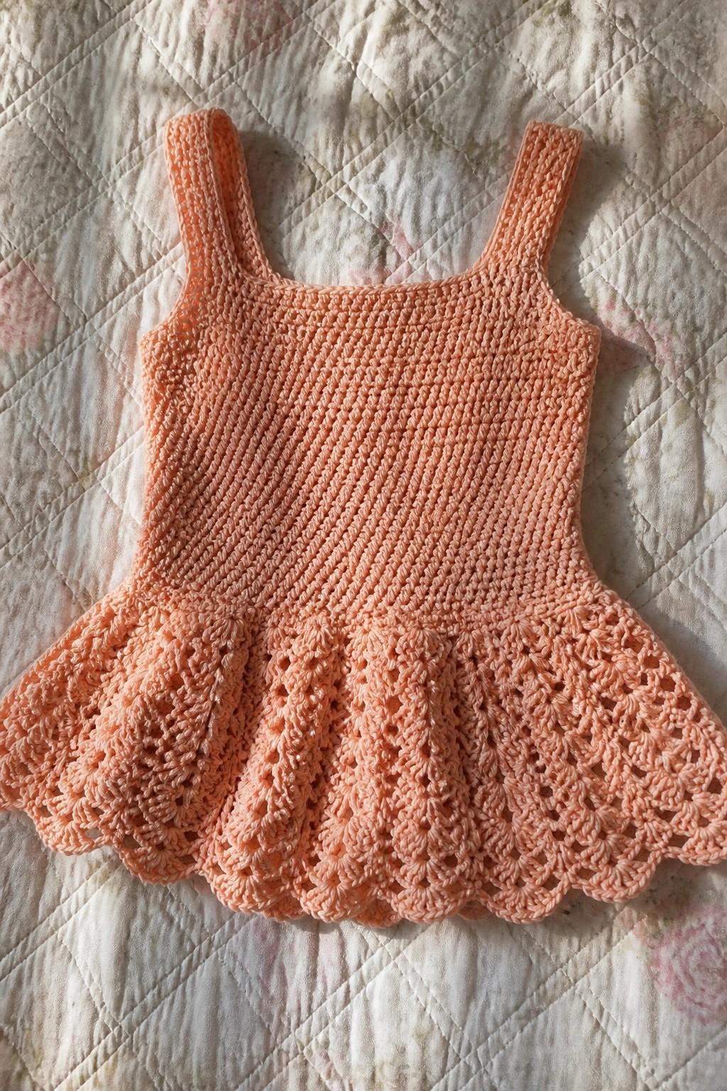 Peach crocheted tank top with straps and scalloped lace hem laid on a quilt.