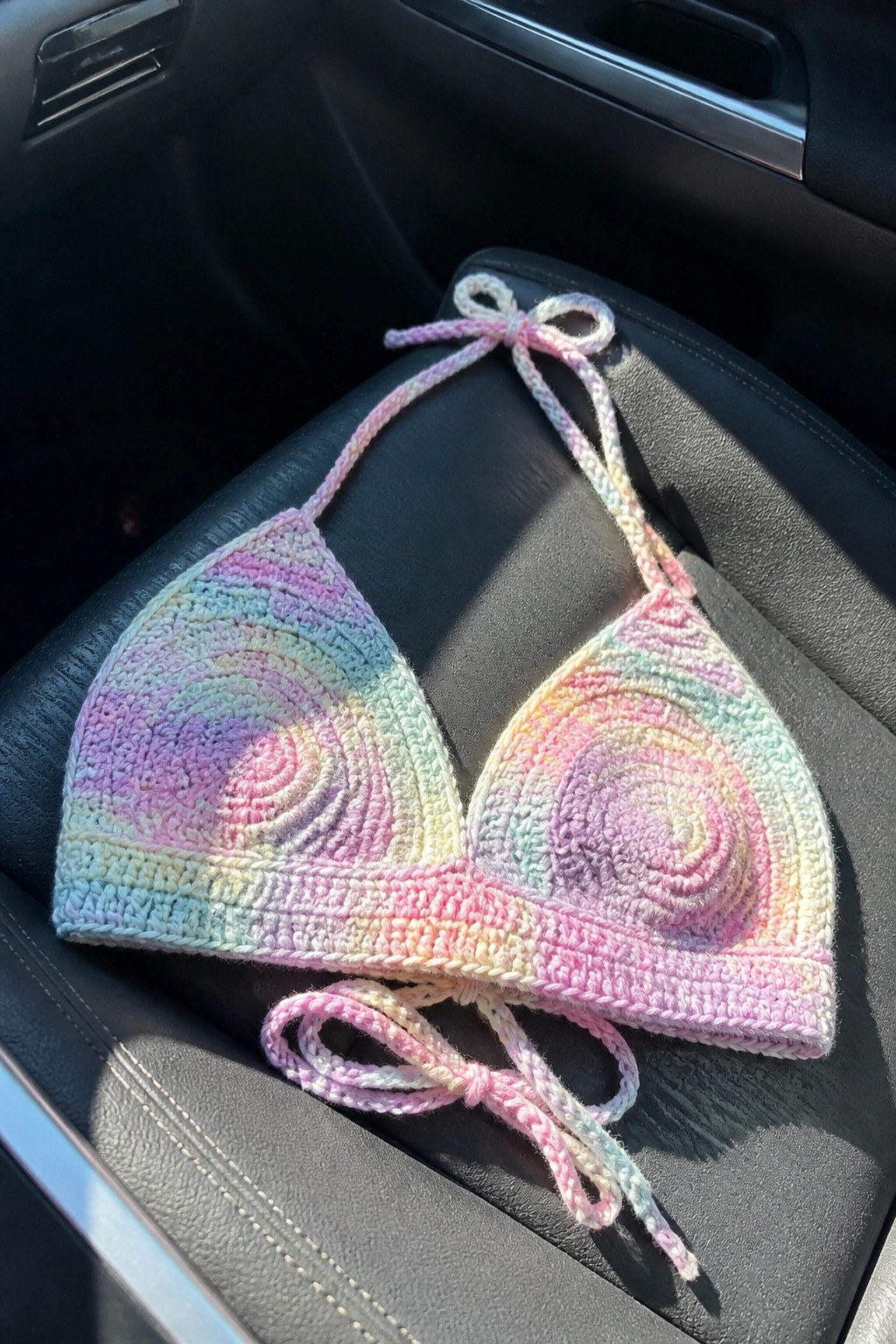 Crocheted pastel rainbow bikini top with ties on black car seat
