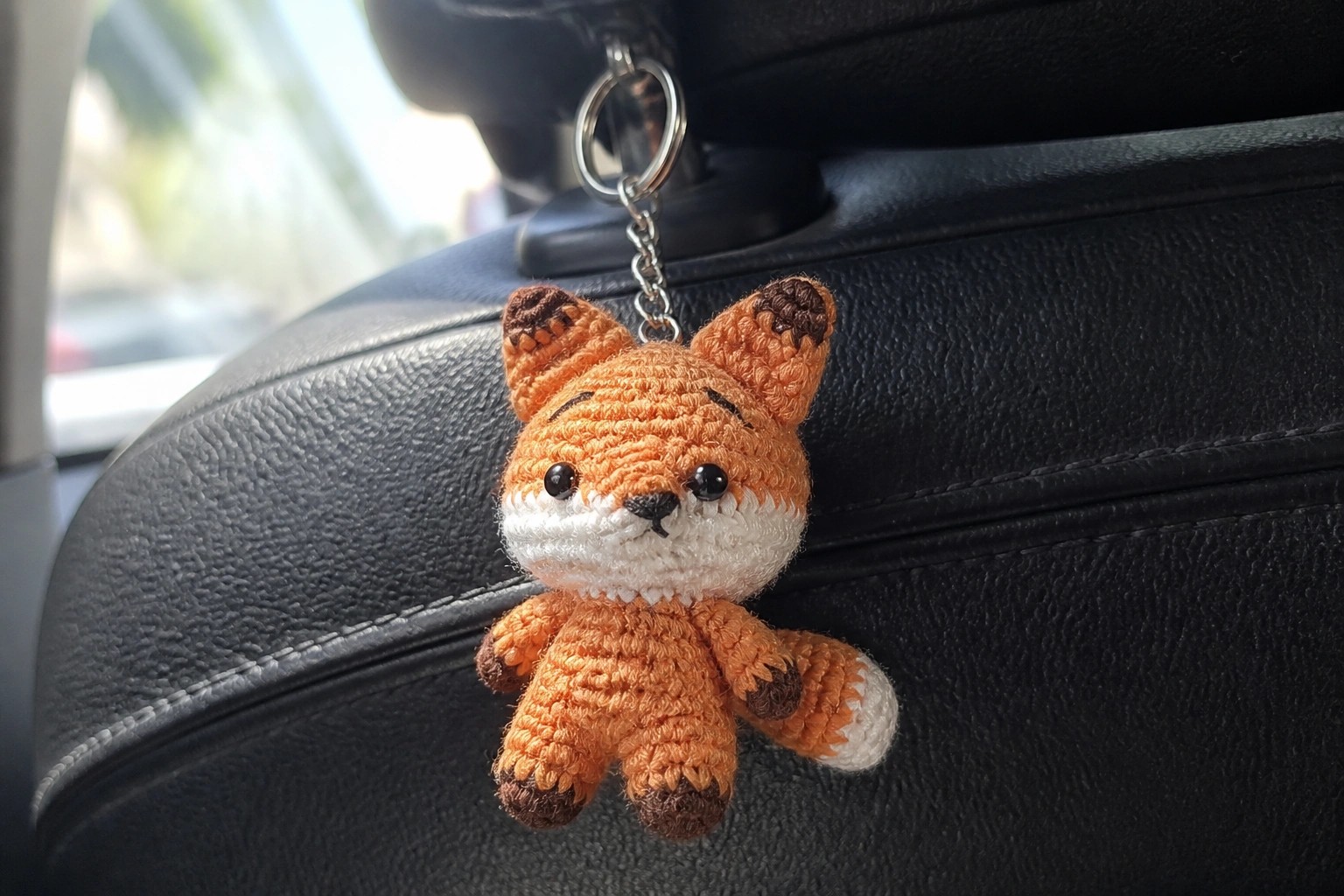 Orange crocheted fox keychain with white face dangling from car headrest.