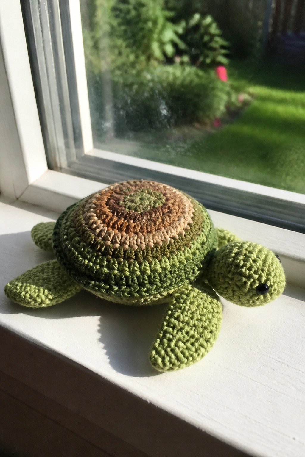 Crocheted green turtle with multicolored shell on sunlit white windowsill