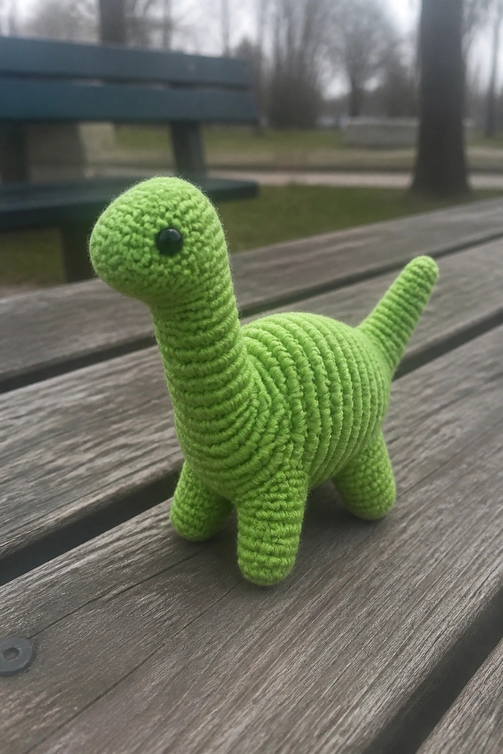 Lime green crocheted dinosaur toy on a weathered wooden park bench