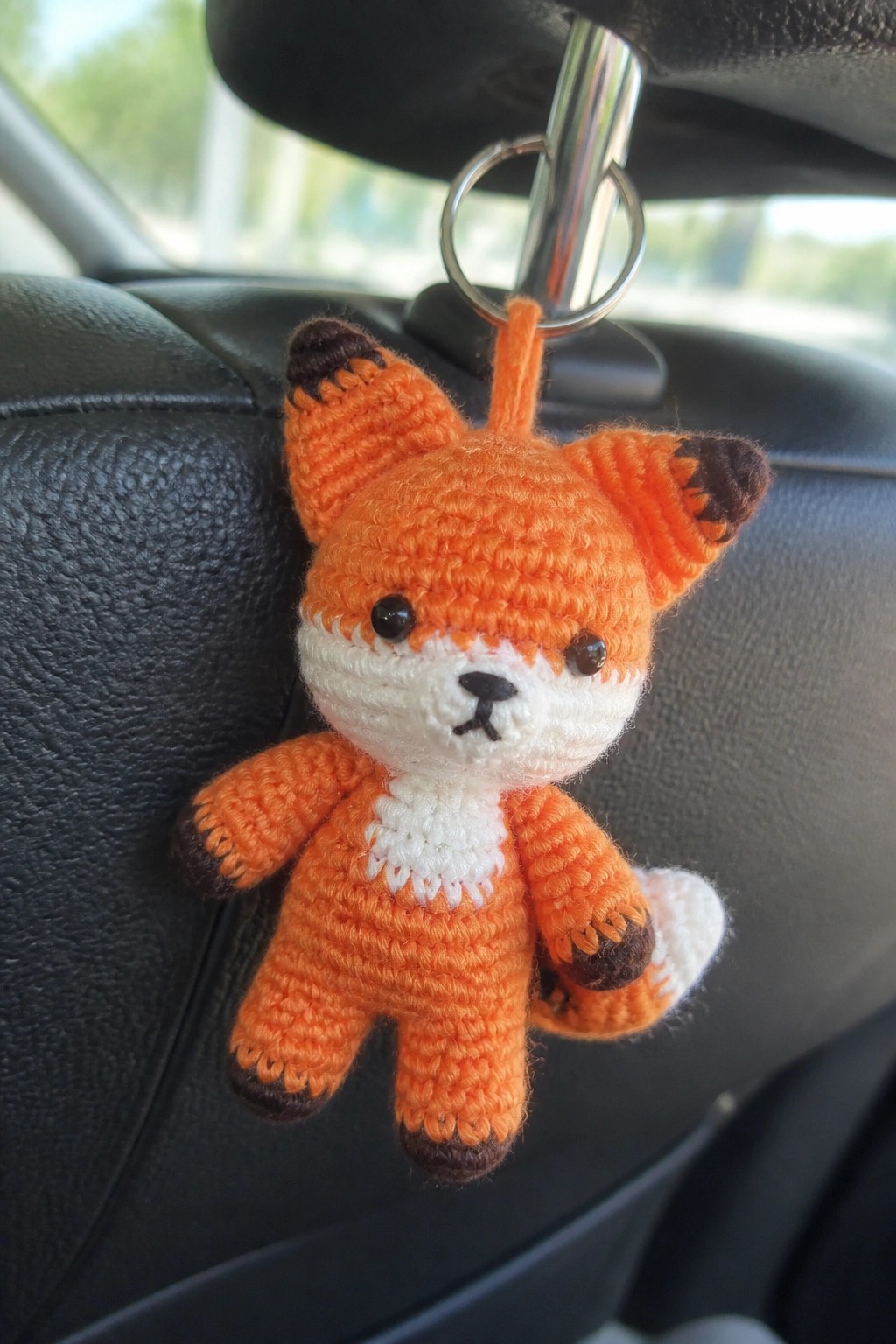 Orange crocheted fox keychain with white face dangling from car headrest.