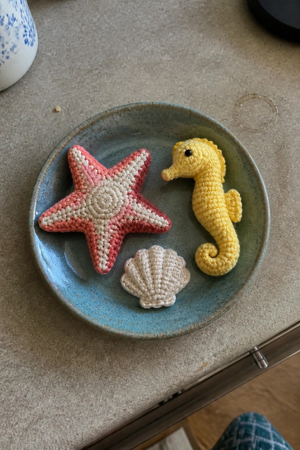 Crocheted pink starfish, yellow seahorse, and white seashell on blue plate