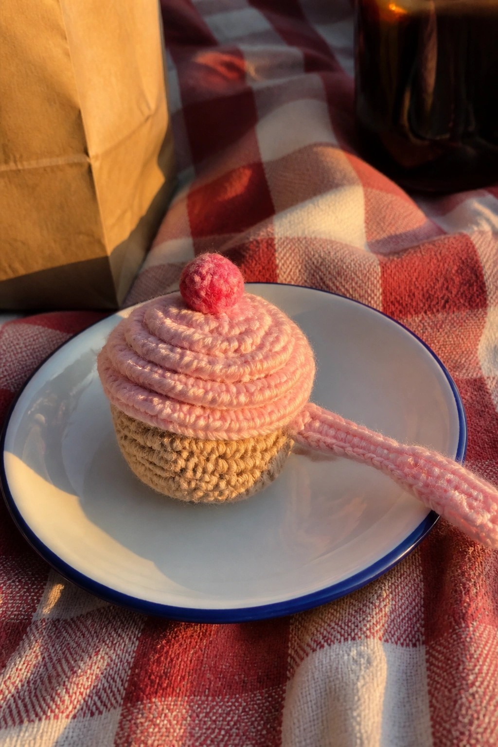 Crocheted cupcake bookmark with pink chain tail on a white plate.