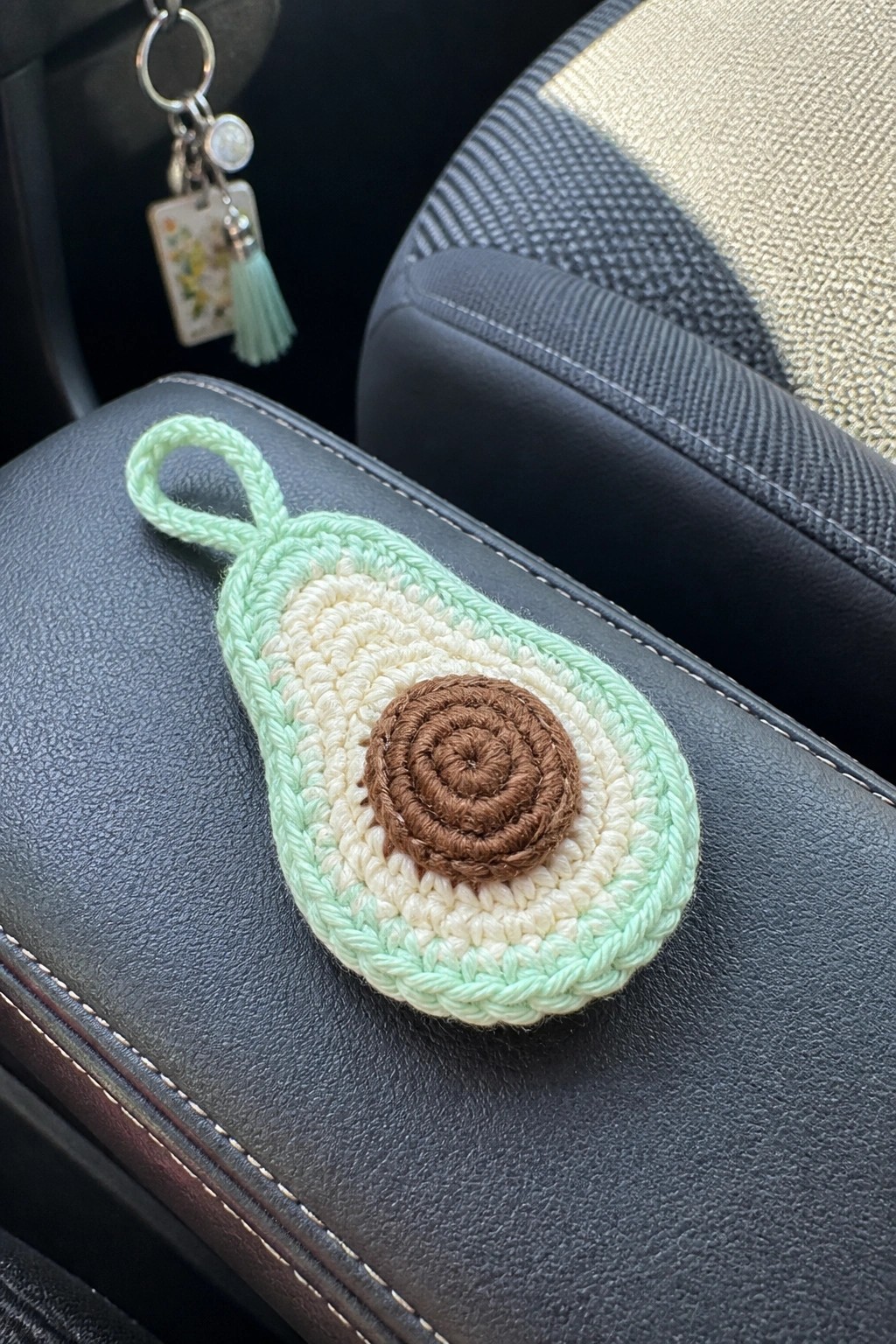 Crocheted avocado keychain with brown pit on black leather car armrest