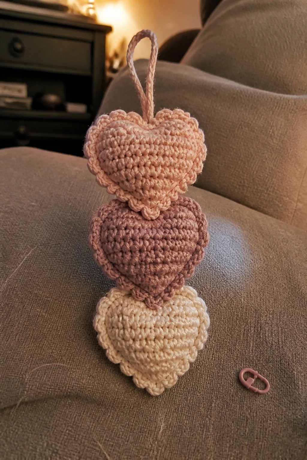 Three crocheted hearts in gradient pink tones stacked on beige upholstery