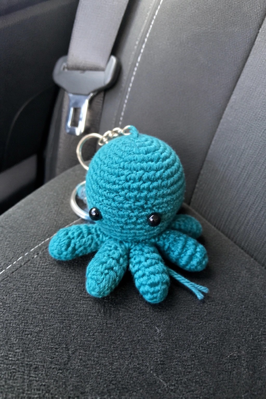 Turquoise crocheted octopus keychain with black eyes on gray car seat