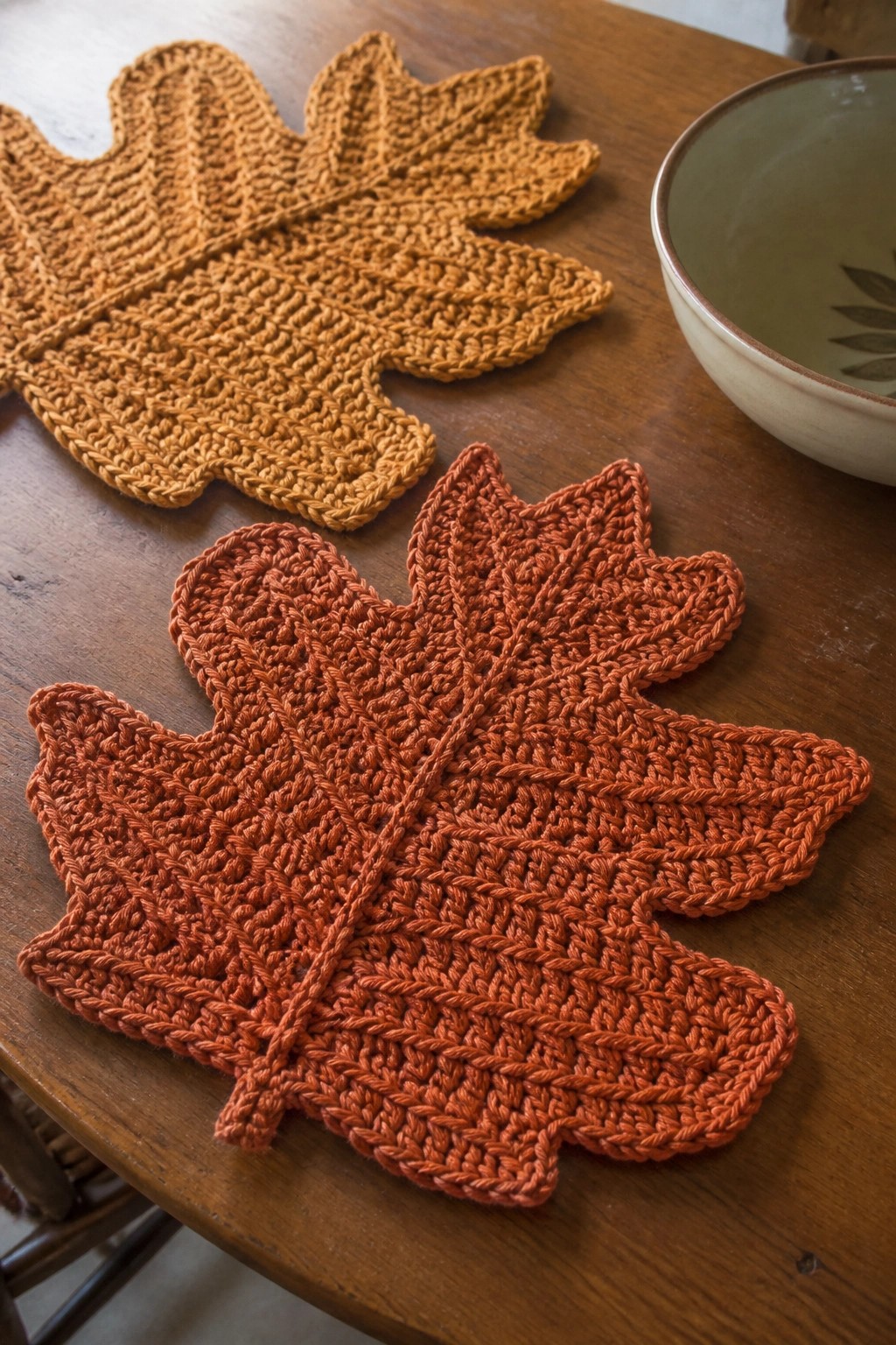 Three crocheted orange maple leaf placemats on wooden table beside ceramic bowl