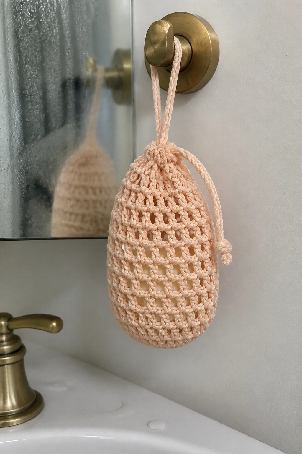 Peach crocheted mesh pouch hanging from brass hook above sink