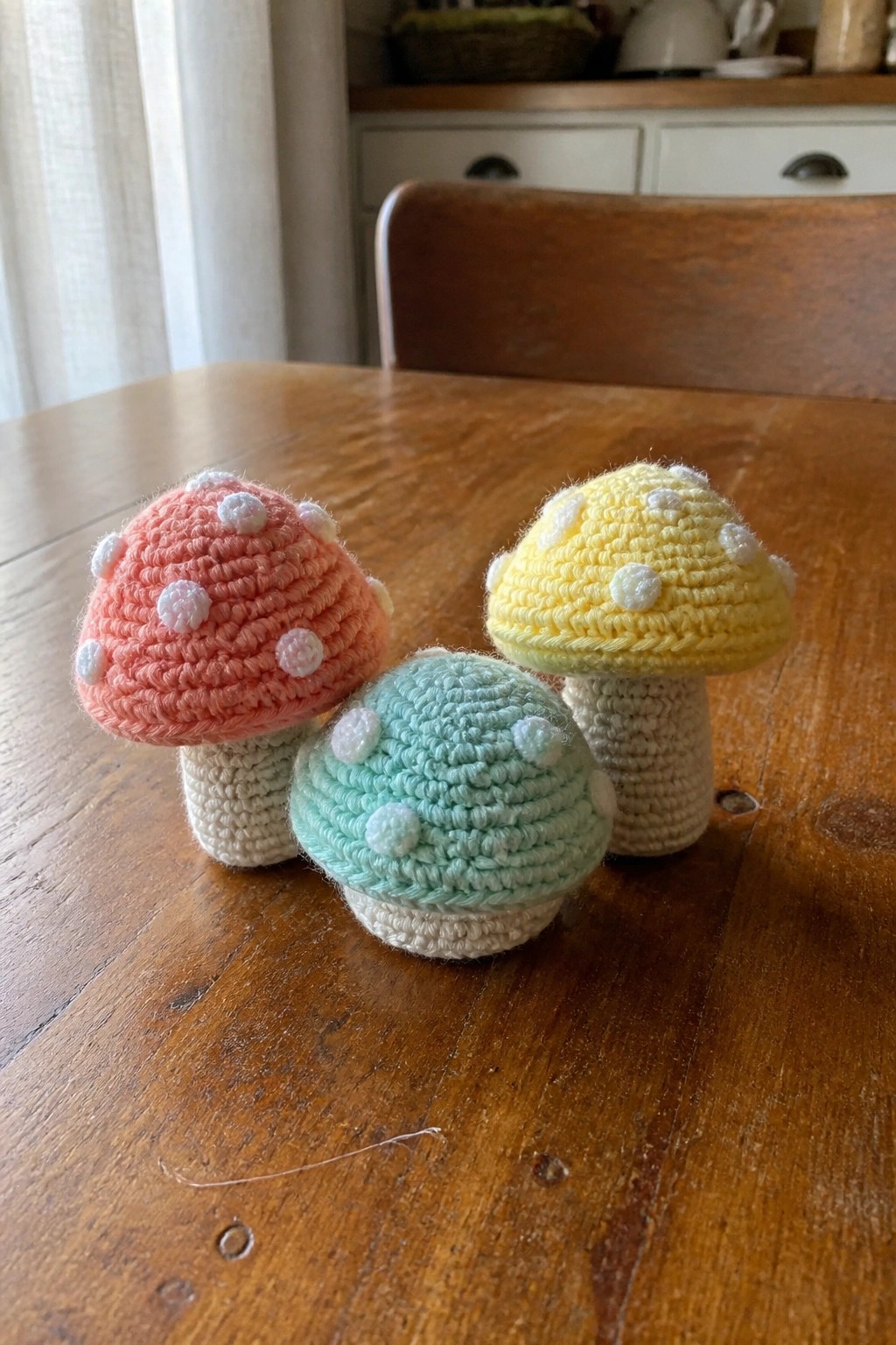 Three pastel crocheted mushrooms with white spots on a wooden table