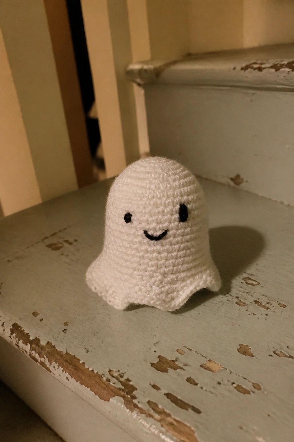 Crocheted white ghost with black eyes and smile on worn wooden stairs