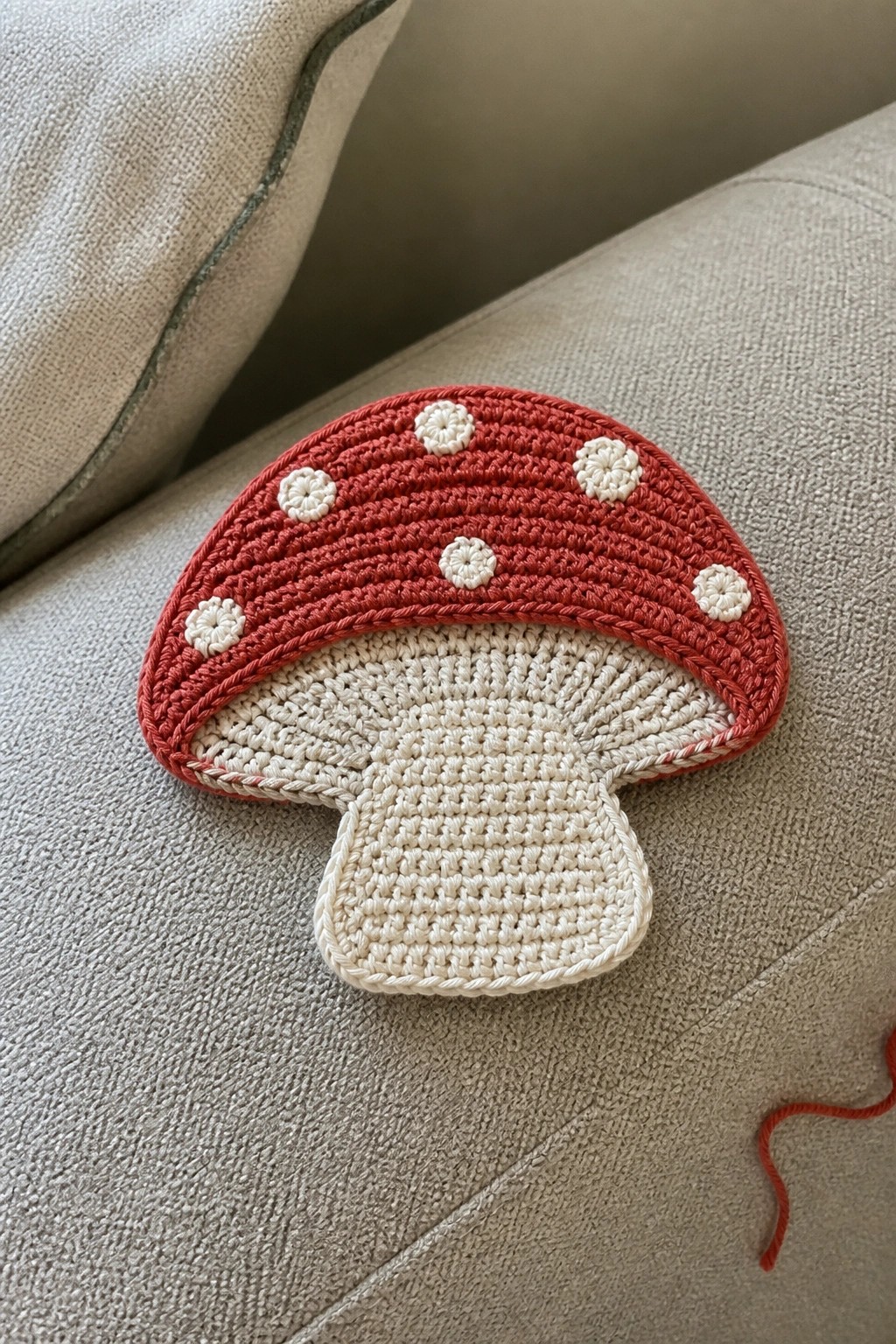 Red crocheted mushroom with white dots on beige couch fabric.