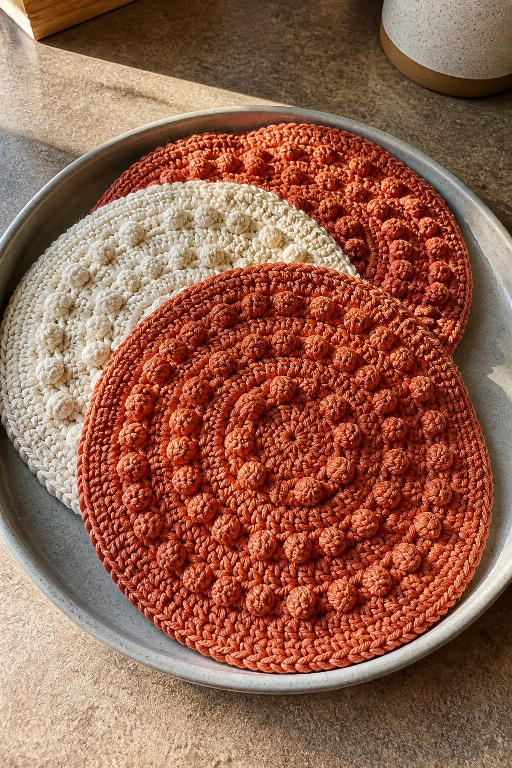 Three crocheted round coasters in orange and cream on a gray plate