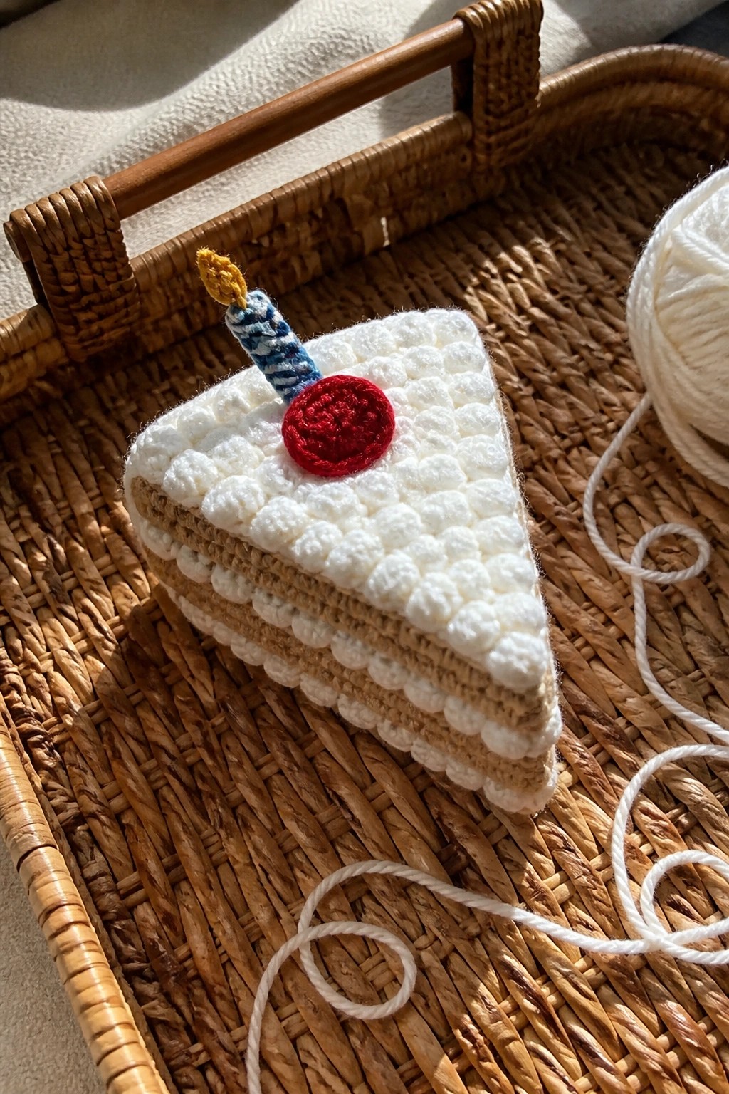 Crocheted cake slice with red cherry and striped candle on woven basket tray